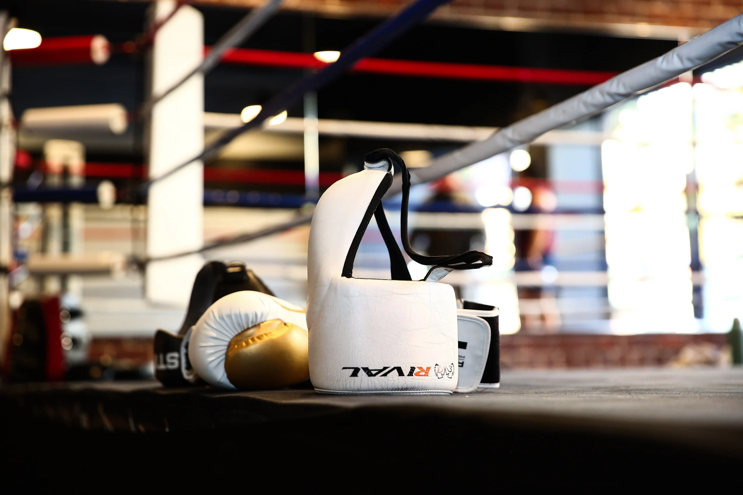 Boxing gloves and white headgear resting beside the ropes of the ring